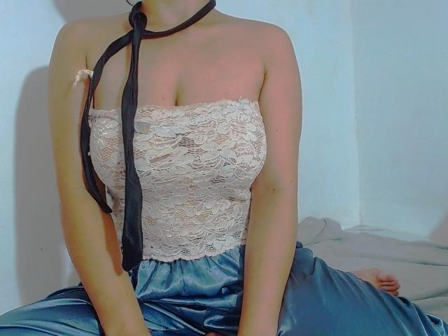 Jenilyn veste uma blusa de renda sem alças, um laço preto amarrado ao redor do pescoço e uma saia azul de cetim brilhante, sentada com os braços para baixo, mostrando seus seios e nádegas à mostra..