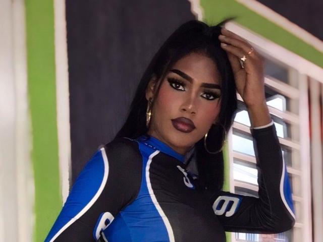 CristinaMontiel with long black hair, dark lipstick, and hoop earrings, wearing a blue and black sports top, hand in hair, looking at camera, showing her tits.