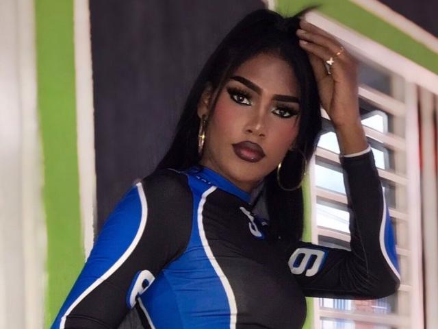 CristinaMontiel with dark skin, long black hair, wearing a blue and black sports outfit, gold hoop earrings, and dark lipstick, hand in hair, looking at camera.