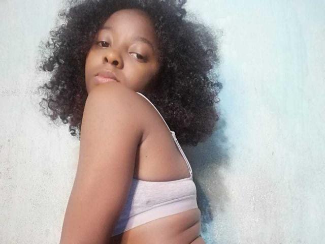 MarfSexy with curly black hair, wearing a white bra, looking over shoulder, showing her small tits, with a slight pout on her brown face.