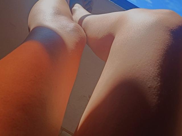 Low-angle shot of JulianaTasty's smooth, shiny, tan thighs and knees, with sunlight highlighting the curves and texture of her skin. Her legs are slightly parted.