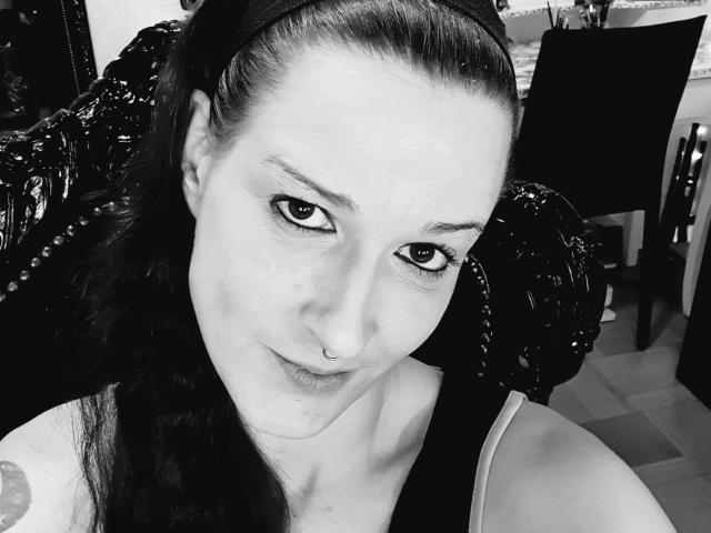 BettyO, con un piercing en la nariz, cabello oscuro recogido en una diadema y un tatuaje en el hombro, mirando a la cámara con una ligera sonrisa. Selfie en blanco y negro..