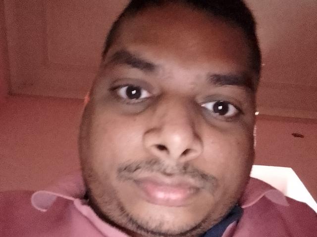 Mihila69 has a dark brown skin tone, short black hair, small goatee, and is wearing a pink hoodie. His eyes are looking directly at the camera.