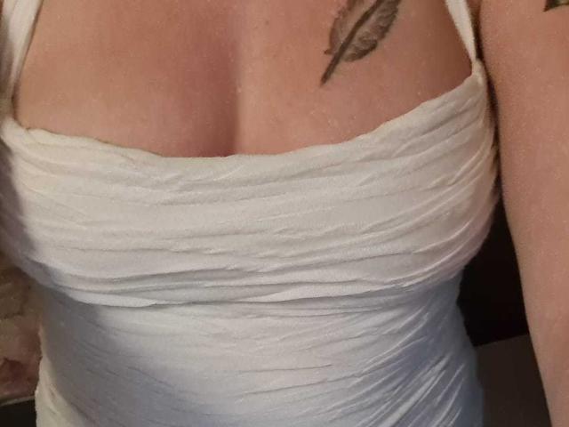 LaCoquinedu69's white, ruched, strapless top shows her large, rounded tits. A small feather tattoo is visible on her right chest. Her skin is light, and she's partially cropped.