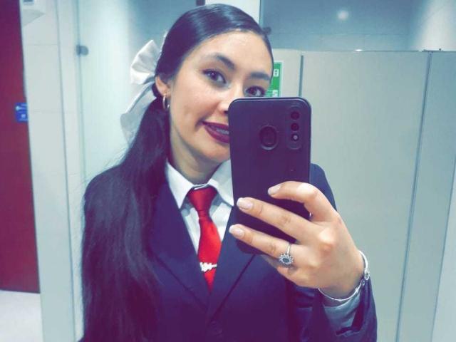 TatianaRiosLove with long black hair, wearing a black suit, white shirt, red tie, and white bow, taking a selfie with a black smartphone, smiling. Boobs, tits, ass not visible.