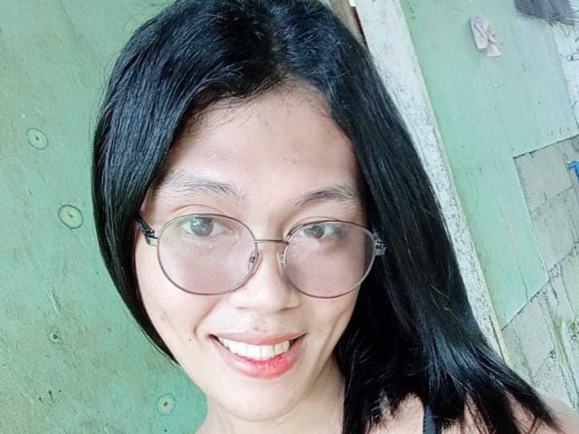 ErikaTS has black hair, glasses, and a smile showing red lips. Her skin is light brown, and she's wearing a sleeveless top. Her tits are small and not visible.