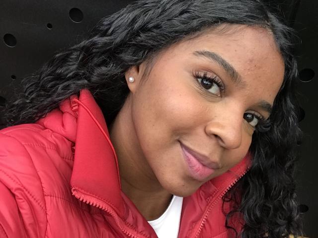 LisaMendez with curly black hair, brown eyes, and a cute smile, wearing a red puffy jacket, small pearl earrings, and a white shirt, showing a slight pimple on her nose.