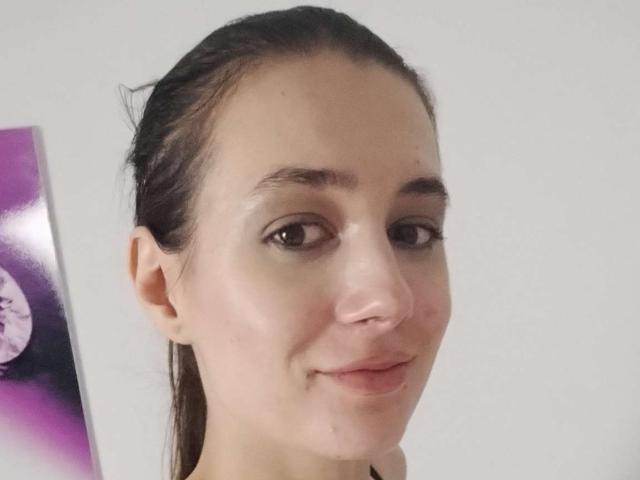 JuliaHuntis with wet, dark brown hair, slightly flushed skin, small nose, and subtle smile, showing brown eyes and small, natural tits in a simple, neutral-colored setting.