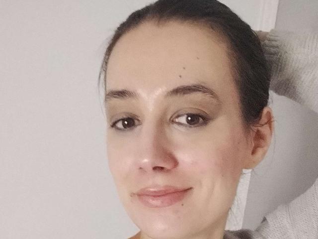 JuliaHuntis has a fair complexion, brown eyes, and a subtle smile with a small mole above her right eyebrow. Her dark hair is pulled back, and she wears a grey sweater.