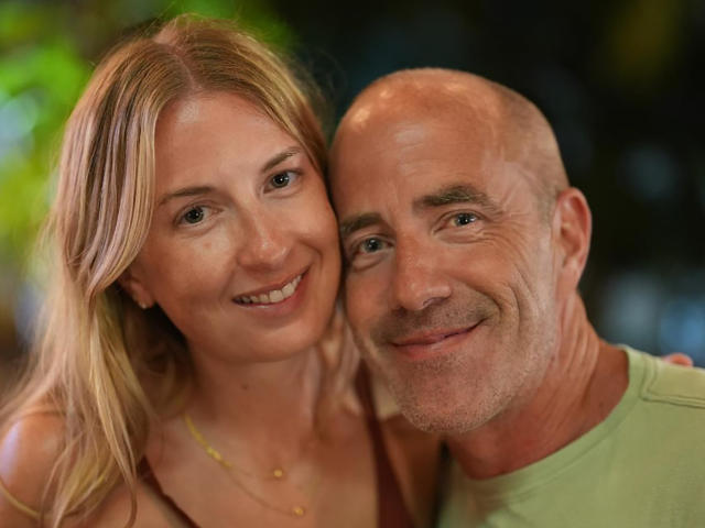 OscarAndRania, a blonde woman with small tits and a bald, gray-bearded man with a cute ass, smiling closely together, both with happy expressions.
