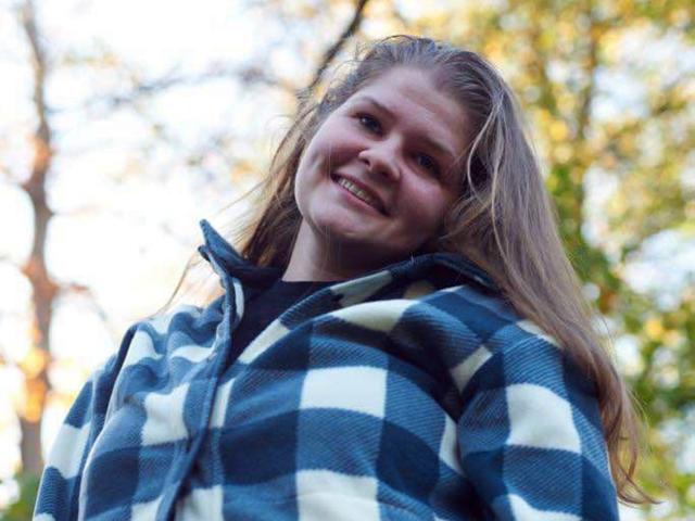 LustCaroline has long, dirty blonde hair, a blue and white plaid shirt, and a slight smile, looking down with a relaxed, cute expression.