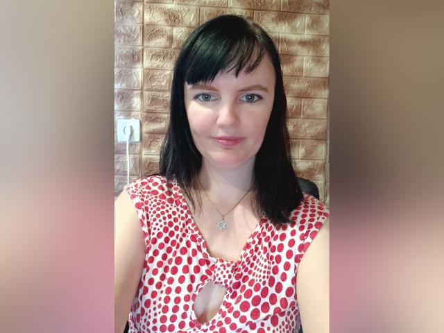AlicexB has black hair, blue eyes, and a pink nose. She wears a red polka dot dress with a keyhole cutout, showing her small tits. She's smiling slightly.