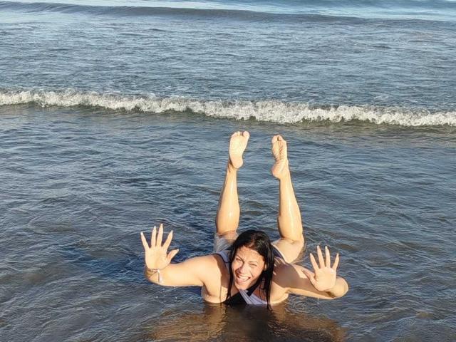 LizaRussell is in the water, flipping upside down with her tits and ass above the surface, smiling, and waving with her hands. Her legs are in the air.