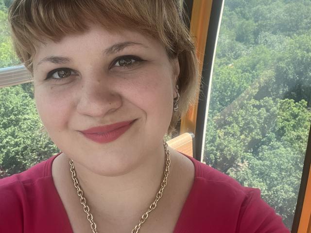AlisaMi has short brown hair, fair skin, red lipstick, small gold chain, and is wearing a pink shirt. She's smiling with her brown eyes. Her tits are small.
