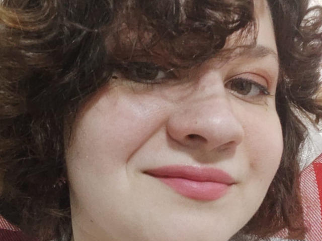 AlisaMi's face with curly brown hair, pink lips, slight smile, fair skin, and brown eyes, showing a cute, relaxed look. Her nose is centered in the image.