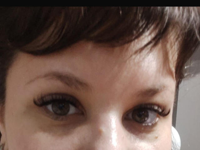 AlisaMi's face, focusing on her eyes, with dark brown hair, thick eyebrows, and long black eyelashes, showing brown eyes and a slight sheen on her skin.