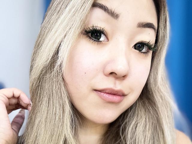 RenyLime has light blonde hair, green eyes, and long eyelashes. She's looking at the camera with a slight smile, showing a small beauty mark near her nose.