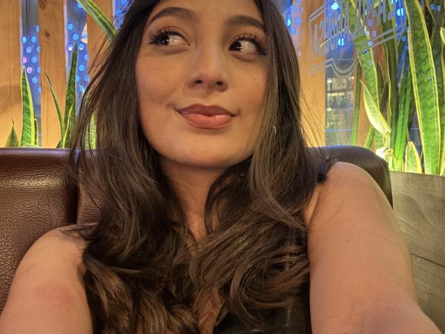 DianaFernandezz with long brown hair, pouty pink lips, and big brown eyes, sitting in a leather booth, looking to the side with a playful, slightly puckered expression.