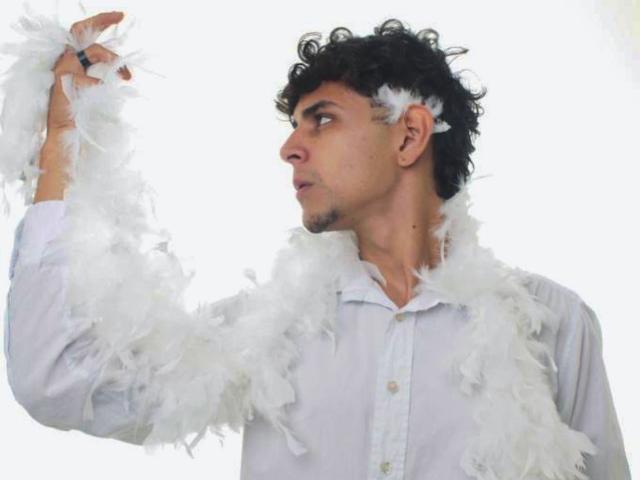 AntonyGaldro with curly black hair, wearing a white feather boa, holding up a feather, white shirt, side profile, looking to the right, slightly pouty expression.