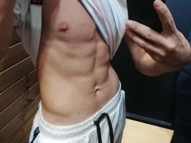 DragMan69's toned, muscular, bare chest with a small, pink nipple, and visible abs, lifting a white shirt, wearing white, loose, drawstring pants, right hand holding shirt.
