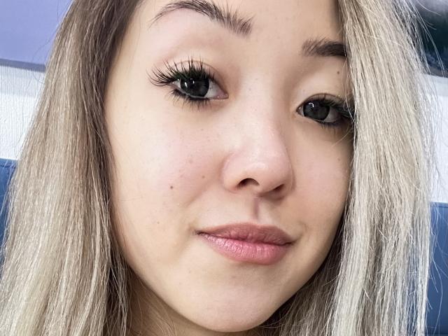 RenyLime's face with blonde hair, black eyelashes, light skin, small freckles, pink lips, and slightly parted mouth in a selfie.