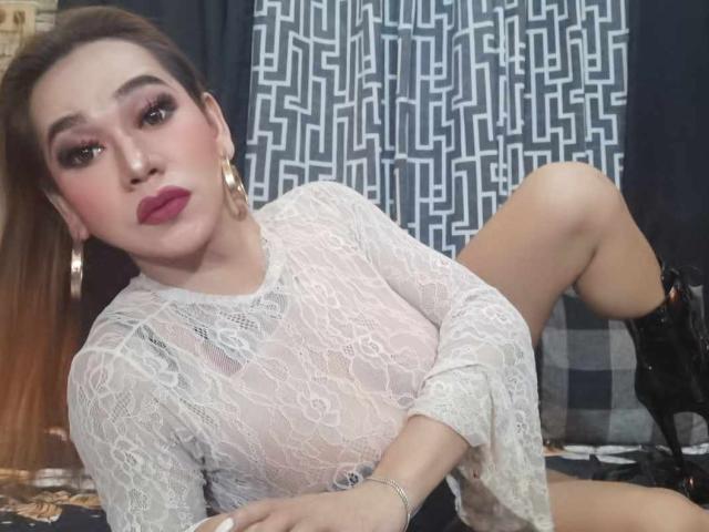 MarianeOhara met lichte huid, bruin haar, rode lipstick, een top met kant, gouden oorbellen, zwarte laarzen, met de benen omhoog, kijkend naar de camera, met make-up, zittend in een ontspannen pose..