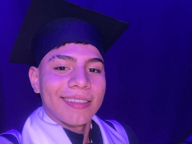 RichiMontes es un joven de piel clara, con una birrete de graduación negra y una toga blanca, sonriendo y con un pequeño piercing en la nariz y un pequeño arete en su oreja izquierda..