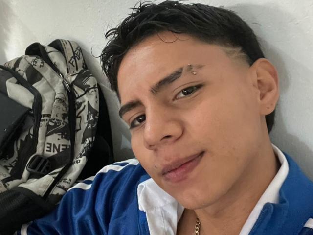 RichiMontes, com cabelo preto curto e molhado, uma pequena piercing no rosto e um casaco esportivo azul e branco, está encostado em uma parede, com luvas ao fundo..