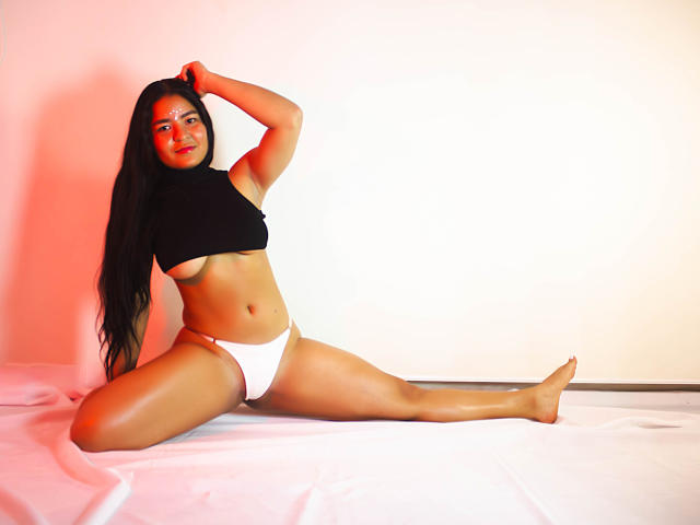 HayamiHot mit langen, schwarzen Haaren, die ein schwarzes Crop-Top und weiße Unterwäsche trägt, sitzt auf einem weißen Tuch, die Beine gespreizt, eine Hand im Haar, und zeigt ihre Brüste und weiße Unterwäsche..