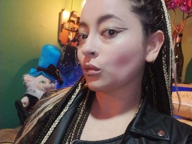 LunaTikka with braided hair, nose ring, and eyeliner, wearing a black leather jacket, pouting with pink blush on her cheeks, and a small lip piercing.