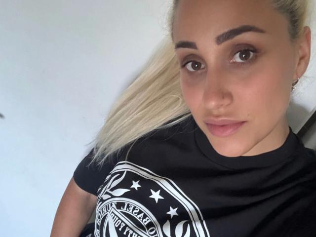 LunaSky-hot has blonde ponytail, thick eyebrows, nose ring, and is wearing a black shirt with a white logo. She has light skin, brown eyes, and subtle pink lips.