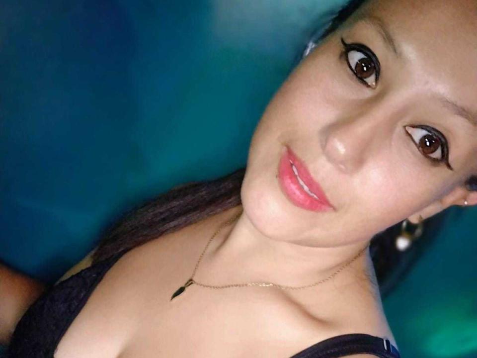 ValeryTits with glossy pink lips, dark eyeliner, and a gold necklace, smiling at the camera, showing her tits in a black top. Her brown eyes are slightly upturned.