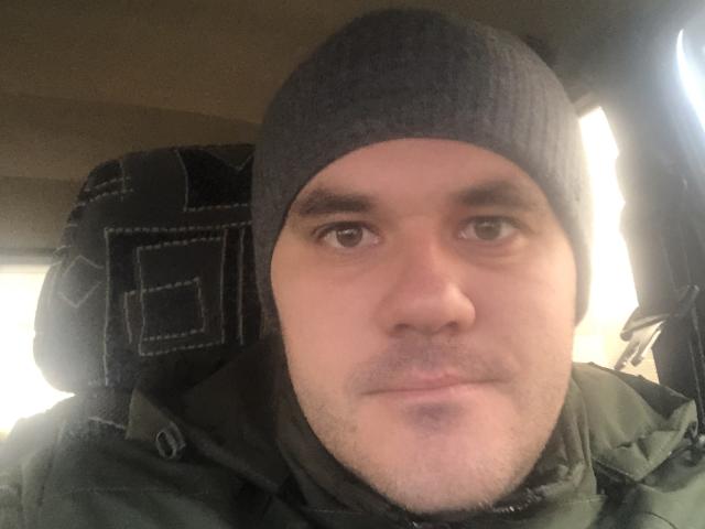 HardWine has a chubby face, light skin, and a black beanie, with brown eyes and a slight mustache. He's wearing a green jacket, sitting in a car.