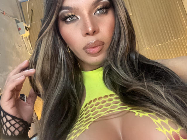 CanelleGarces with long dark hair, eyes closed, wearing a choker and leather glove, touching her lips with a finger. Black and white, sexy, elegant, and confident.