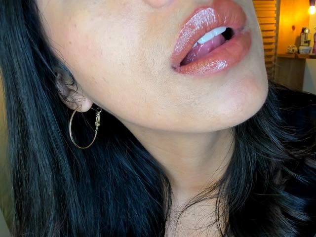 Les lèvres roses et brillantes d'EimyRousse sont légèrement entrouvertes, laissant entrevoir un soupçon de sa langue. Elle porte des boucles d'oreilles dorées et a les cheveux noirs et ondulés. Sa peau est claire et présente quelques taches de rousseur..