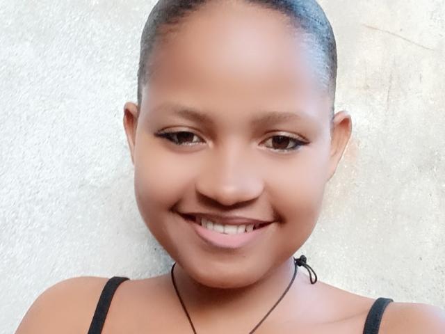 MeriAndMark has a cute smile with small brown eyes, a black hair bun, and is wearing a black strap top, showing a slight tan and a small black necklace.