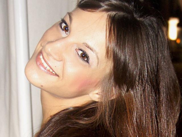 CassandraMichelli's smiling face with brown eyes, glossy pink lips, and dark brown hair. She's turning her head, showing a cute mole on her left cheek.