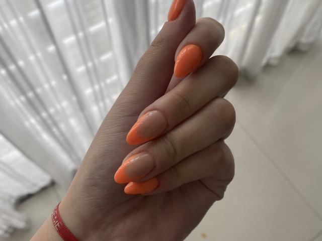 AlexaLip's hand with long, shiny orange nails on pale skin, fingers slightly curled, wearing a red bracelet, light coming from the side.