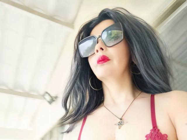 BrandyMostHottest with black hair, red lipstick, large tits, red lace bra, hoop earrings, and reflective sunglasses, wearing a star necklace, looking up confidently.