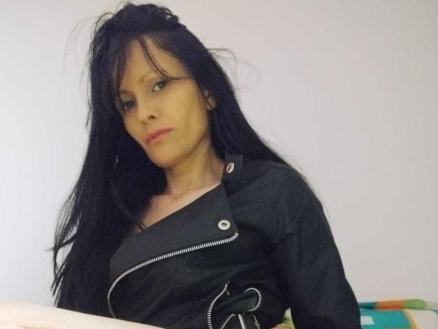 DulceHotShary with long black hair, wearing a black zip-up shirt, looking slightly to the side with a neutral expression, small breasts, and a light skin tone.