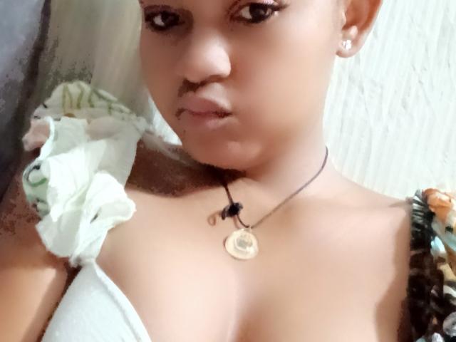MeriAndMark has light brown skin, a small mustache, and a necklace with a gold pendant. She's wearing a white top with floral straps, showing her tits.