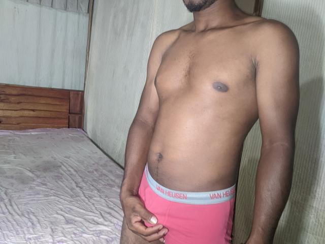 MeriAndMark is a dark-skinned, muscular dude with a trimmed beard, wearing pink VanHeisen underwear, showing his flat chest and hand on his bulge.