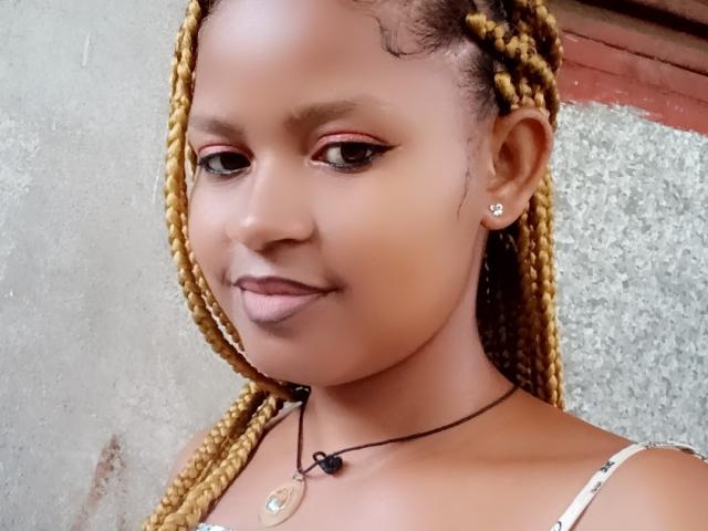 MeriAndMark has brown braids, dark pink eyeliner, and a small smile. She wears a necklace with a circular pendant and a cute ear stud. Boobs are not visible.