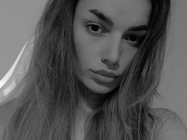 Black and white selfie of IngridI with long, wavy hair, pouty lips, and a slight nose piercing, topless, showing small tits with a nipple piercing.