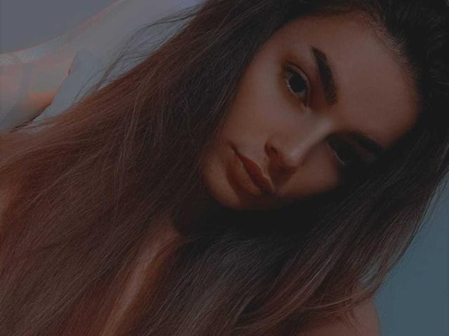 IngridI has long brown hair, brown eyes, and a serious expression, looking slightly to the side with her nose close to the camera. She's topless, with her tits barely visible.