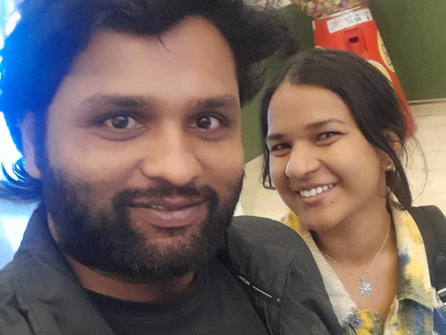 Xander has a black beard and mustache, medium brown skin, and dark hair. Cecile has light brown skin, black hair, and is smiling with her teeth showing.