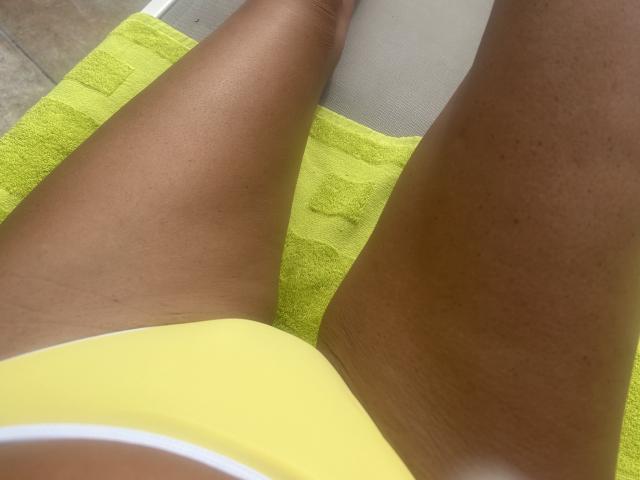 BlackAngeel's dark brown thighs, wearing yellow bikini bottoms, resting on a green towel, taken from a top-down angle, showing her smooth skin and slight tan lines.