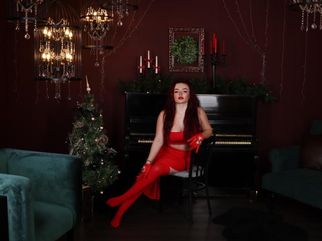 NicolPots with red lipstick, wearing a red tube top, matching skirt, and gloves, sitting on a chair, showing her tits, in a dark room with a Christmas tree.
