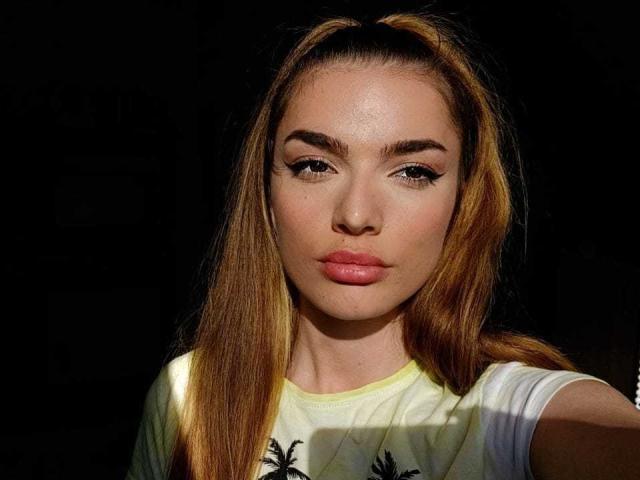 IngridI has light brown hair in a high ponytail, full lips, and thick eyebrows. She wears a yellow shirt, and her face is illuminated by sunlight.