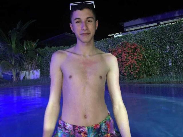 ThomasTwink69 est un jeune homme mince, avec un visage mignon, de petites seins, et un pénis flasque et non circoncis, portant un maillot de bain à fleurs, debout dans une piscine la nuit..